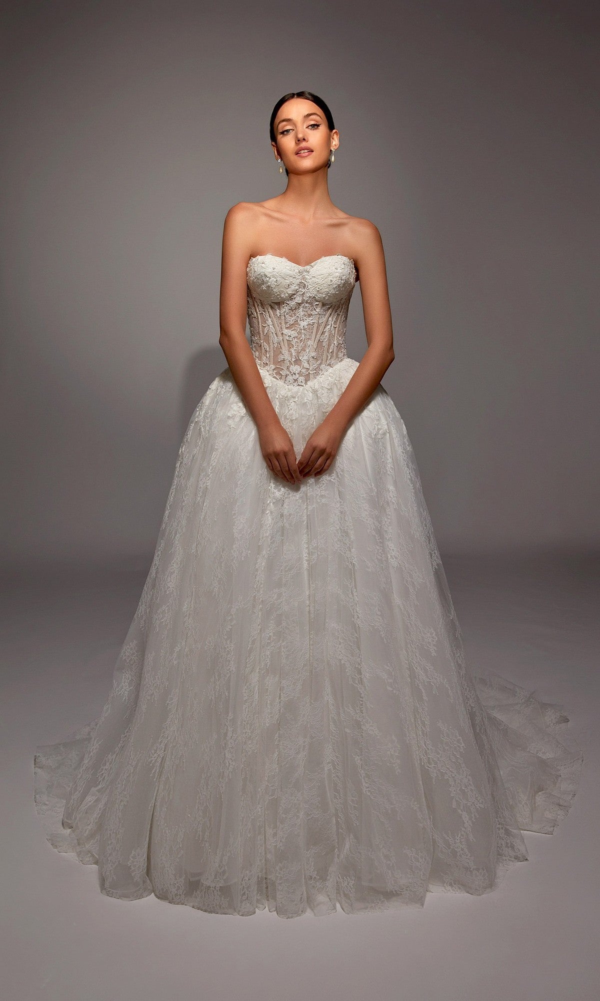 A woman poses gracefully against a plain, neutral background in the Alyce 7163 long white dress, featuring a strapless fitted bodice and full ball gown skirt.
